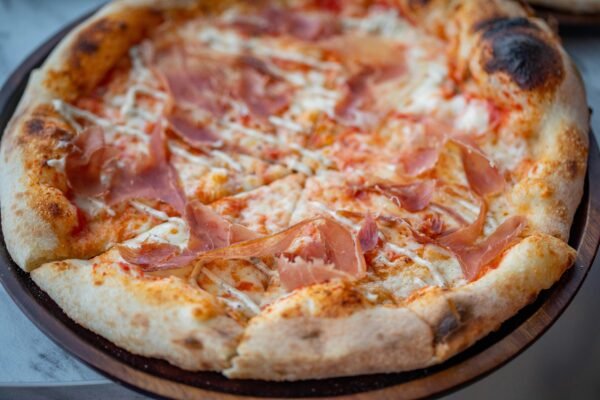 Close-up of a freshly baked prosciutto pizza with melted cheese on a wooden platter.
